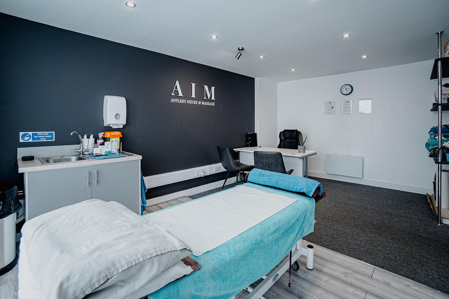 The treatment room at Appleby Injury & Massage, with a made-up treatment couch below the AIM signage.