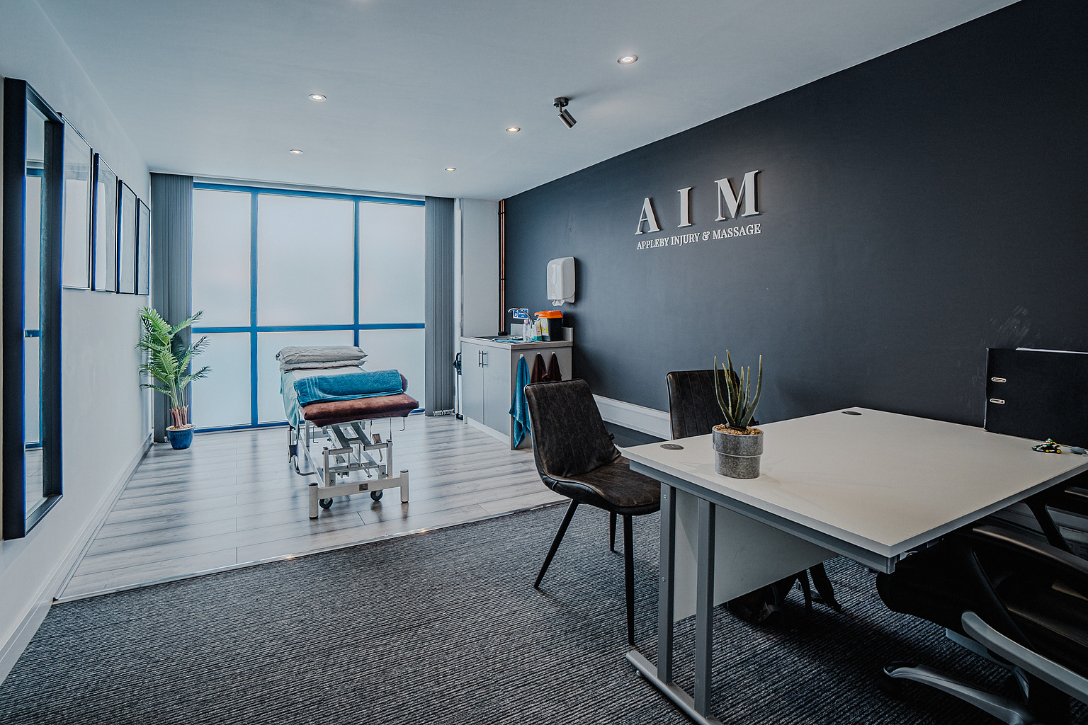 The consultation desk at Appleby Injury & Massage, with the treatment couch and AIM signage beyond.
